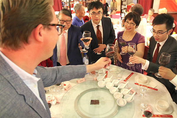 Vijf personen staan rond een tafel en proosten met een glas rode wijn